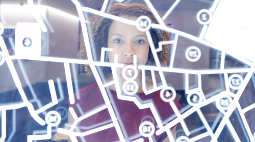 A imagem é uma foto com intervenção gráfica. Uma mulher está de pé, olhando para um vidro com códigos de computador desenhados.