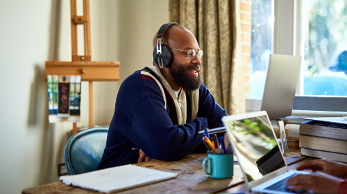 A imagem é uma foto. Em um ambiente de escritório, um homem negro está sentado, olhando algo no computador a sua frente.